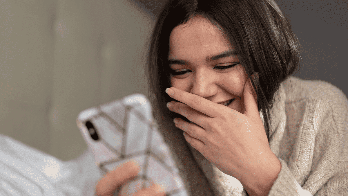 A girl reading a text message and smiling while lying on the bed