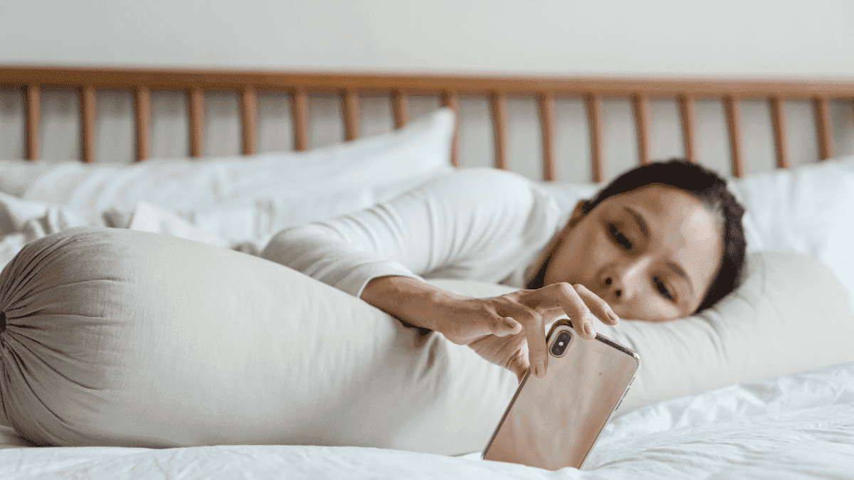 A girl using her phone while lying down in her bed