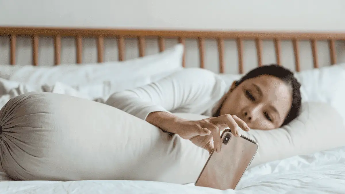 A girl using her phone while lying down in her bed