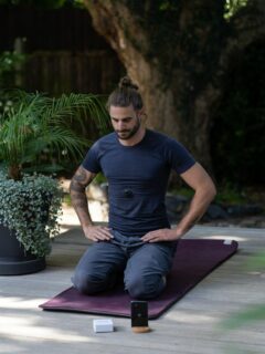 a man sitting on a yoga mat with his hands in his pockets